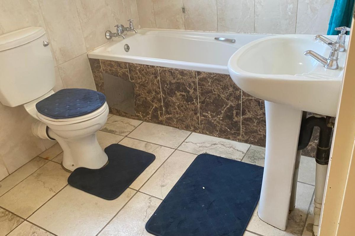 A functional bathroom featuring a pedestal basin, a standard bathtub with tiled surround, and a toilet, finished with neutral wall and floor tiling.