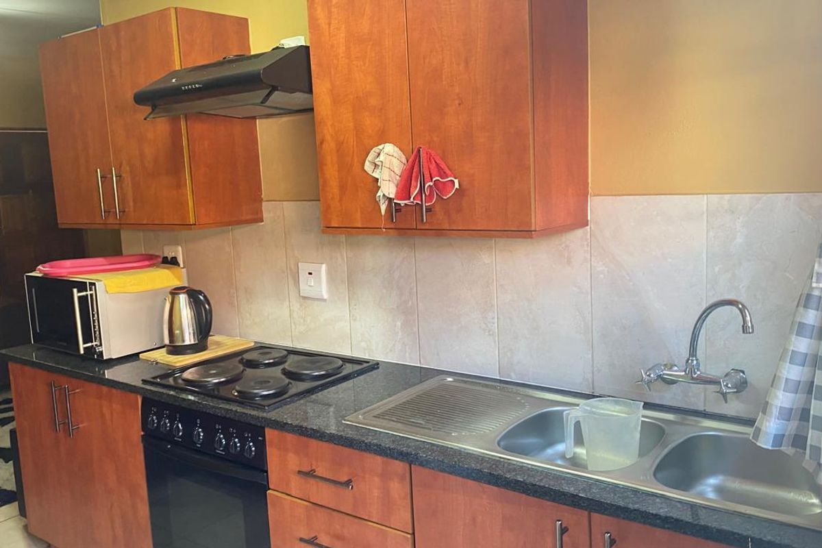 A functional kitchen featuring wooden cabinetry, a built-in oven with electric hob, extractor fan, and a double-basin stainless steel sink with tiled backsplash.