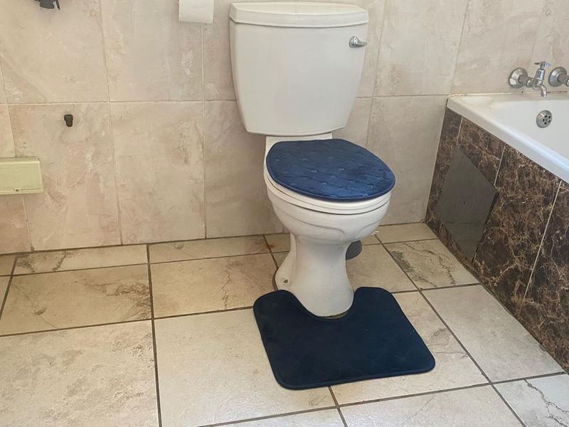 A functional bathroom featuring a standard toilet, tiled flooring, and a bathtub with dark marble-effect side paneling.