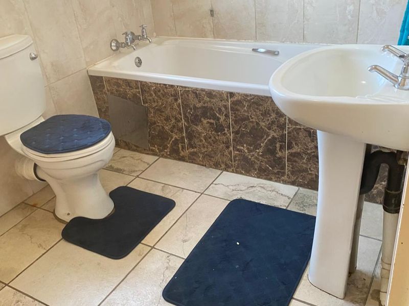 A functional bathroom featuring a pedestal basin, a standard bathtub with tiled surround, and a toilet, finished with neutral wall and floor tiling.