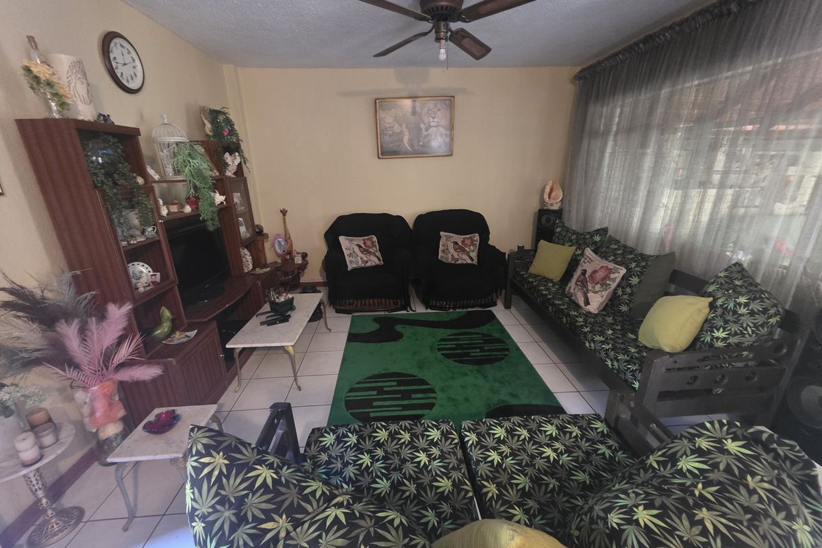 A living room featuring tiled flooring, a ceiling fan, and large windows with curtains, providing a functional and lived-in space.