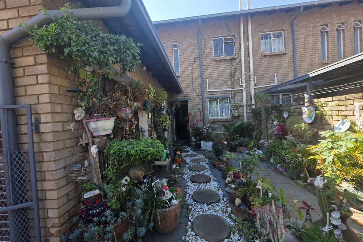 A private rear courtyard area featuring brick paving, a stone pathway, and established garden beds against a face-brick townhouse exterior.