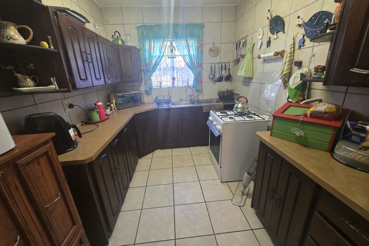 A functional kitchen featuring dark wood cabinetry, tiled flooring, a double sink, and a freestanding gas stove.