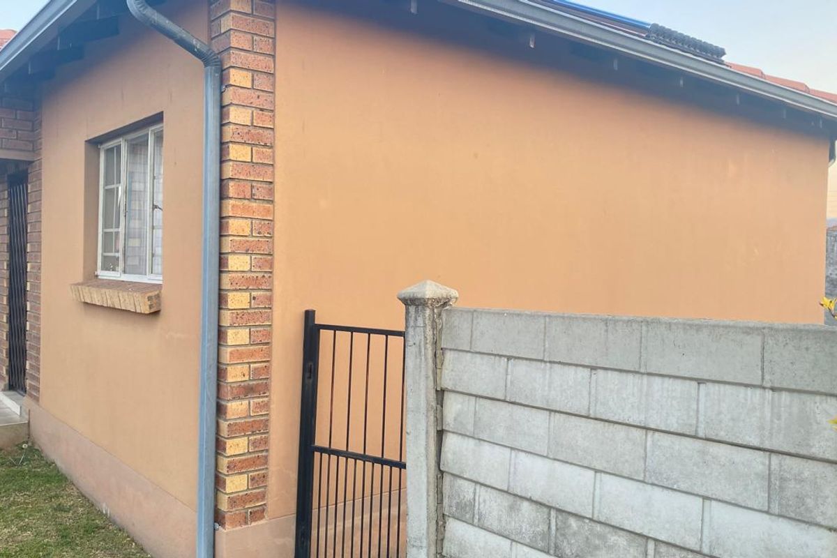 Exterior view of the townhouse featuring a plastered facade, brick corner detailing, tiled roof, and a concrete block boundary wall with a metal gate.