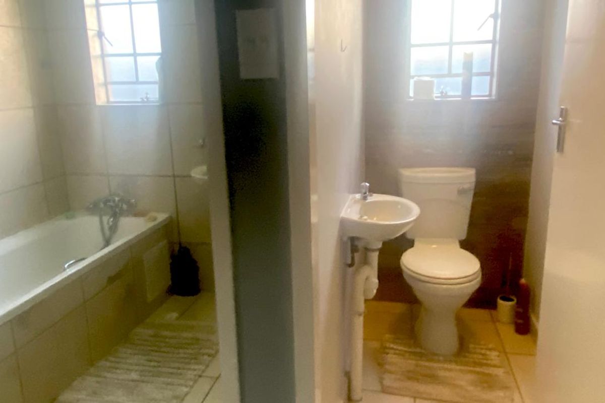A functional bathroom featuring a bathtub, a wall-mounted basin, and a toilet, finished with neutral wall and floor tiles.