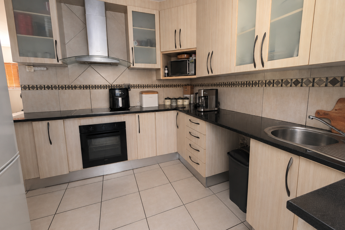 A functional kitchen featuring light wood-toned cabinetry, black granite countertops, a stainless steel extractor fan, built-in oven, and tiled flooring.