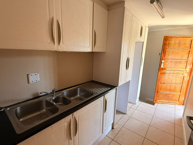 A functional kitchen area featuring laminate cabinetry, a double bowl stainless steel sink, tiled flooring, and direct access via a timber door.