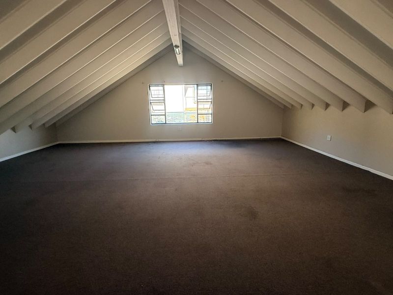 Spacious attic-style bedroom featuring a high pitched ceiling with exposed timber rafters and a central window, offering a versatile blank canvas.