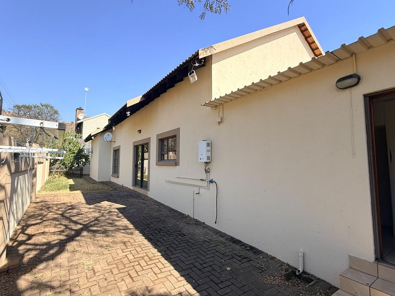 Rear exterior view of the property featuring a paved walkway, gas geyser installation, and access via a sliding door.