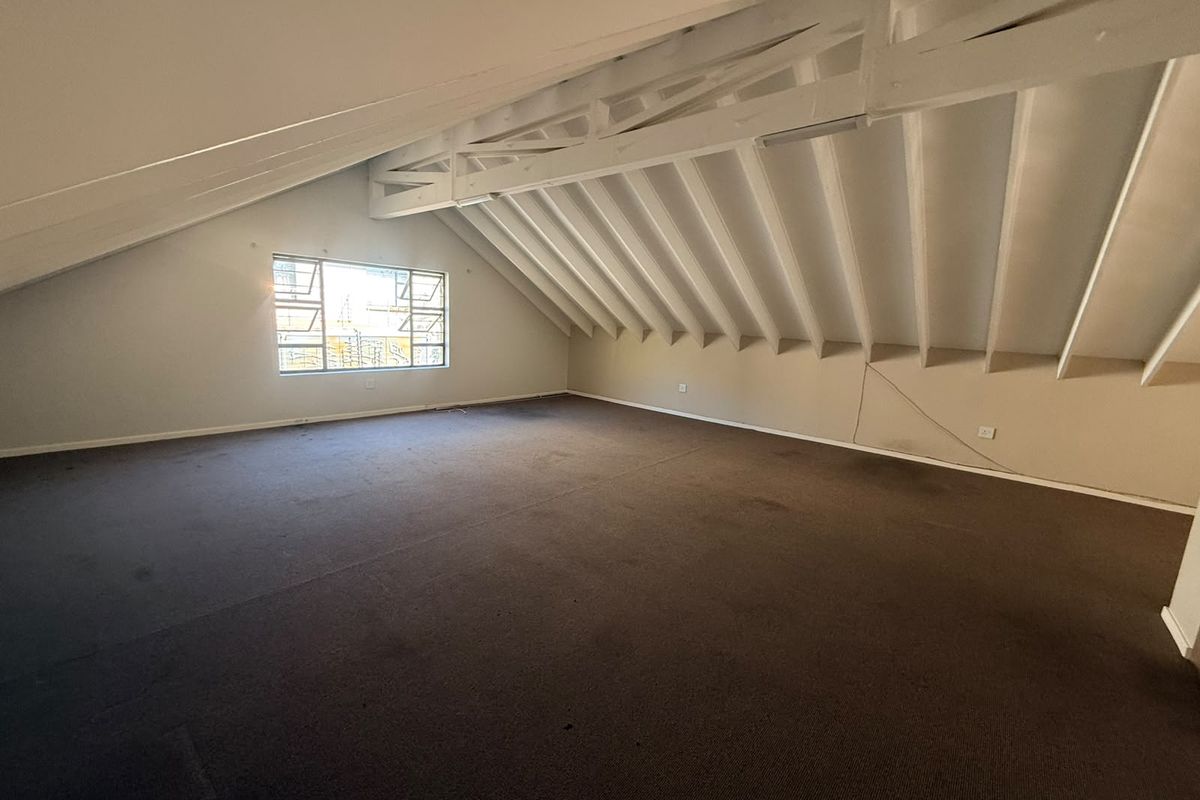 Spacious attic-style bedroom featuring exposed timber rafters, a pitched ceiling, and a large casement window, offering a versatile blank canvas for renovation.