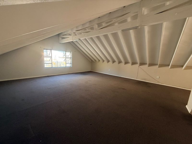 Spacious attic-style bedroom featuring exposed timber rafters, a pitched ceiling, and a large casement window, offering a versatile blank canvas for renovation.