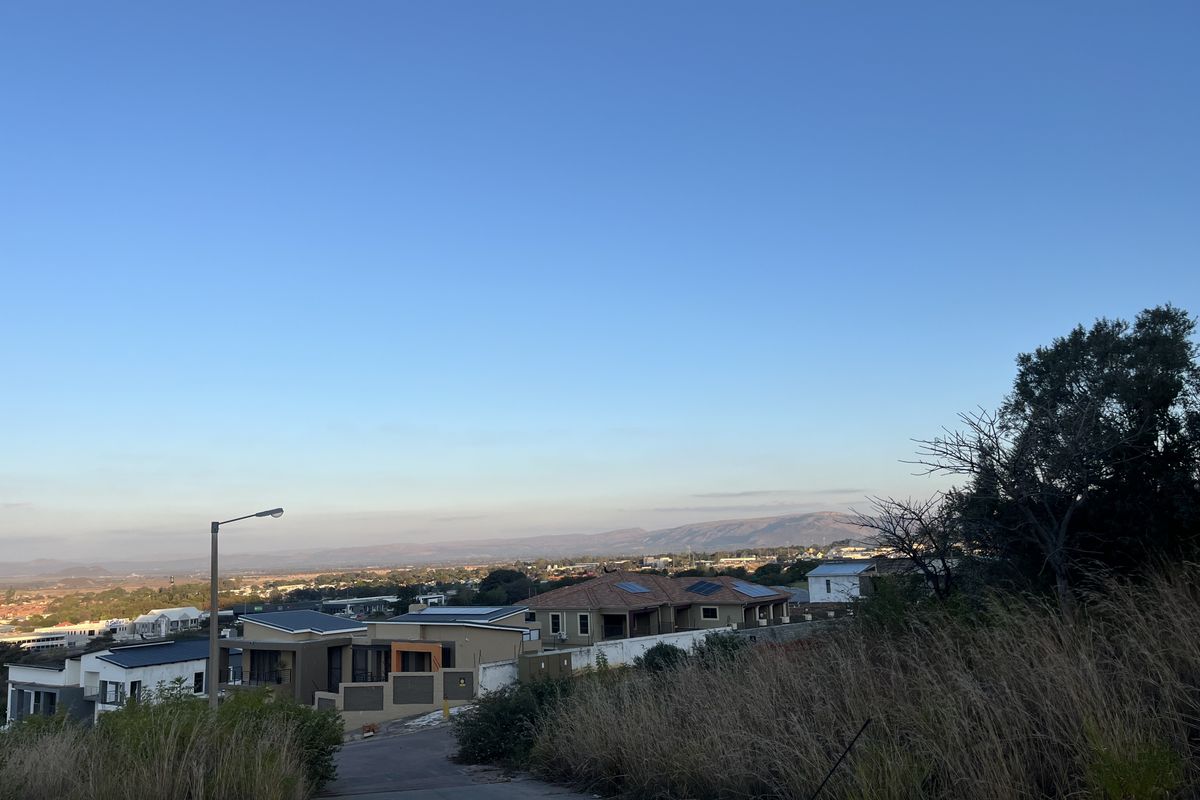 Elevated view overlooking a residential neighborhood and distant mountain landscape from a paved access road.
