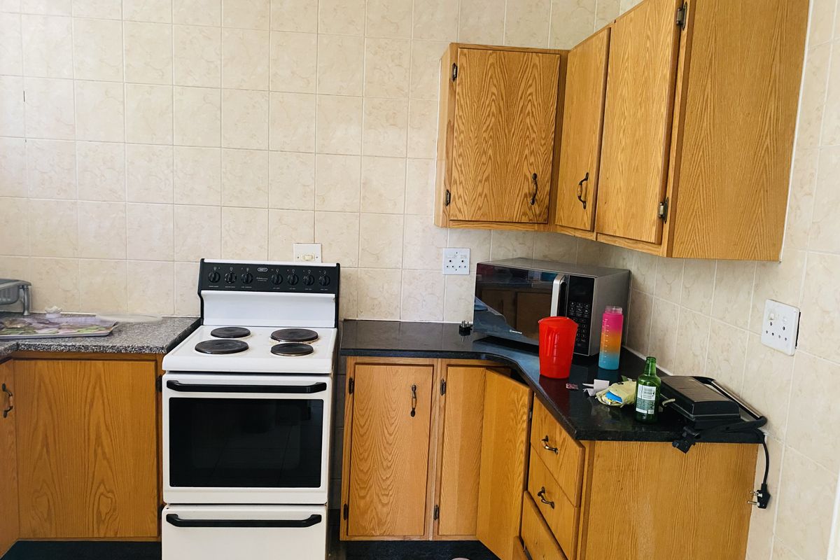 A dated kitchen featuring wooden cabinetry, granite countertops, and a freestanding electric stove with tiled splashbacks.