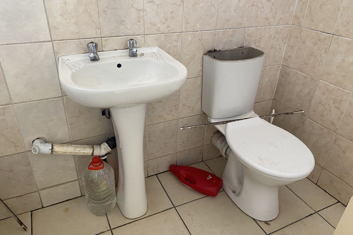 A basic bathroom featuring a pedestal basin and toilet with tiled walls and flooring, currently requiring maintenance and cosmetic updates.