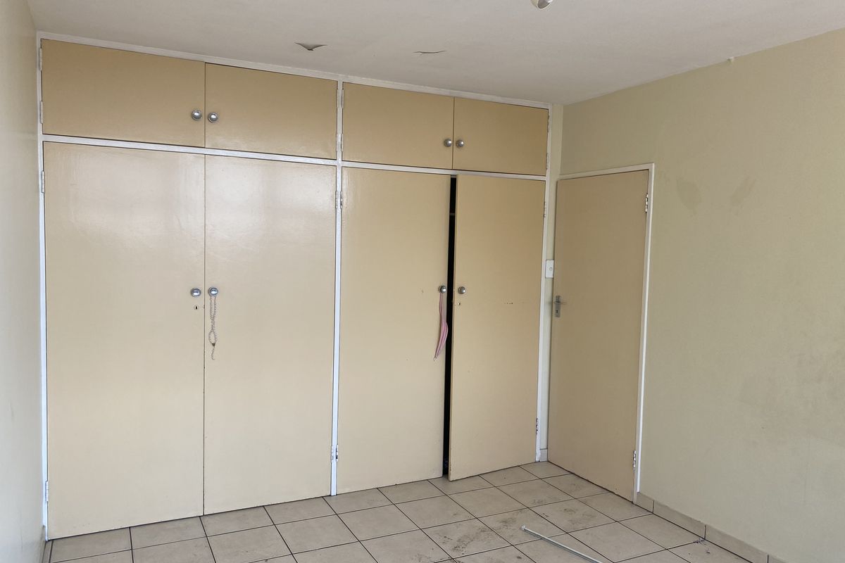 An empty bedroom featuring built-in cupboards, tiled flooring, and a neutral color palette, requiring minor cosmetic updates to restore its appeal.