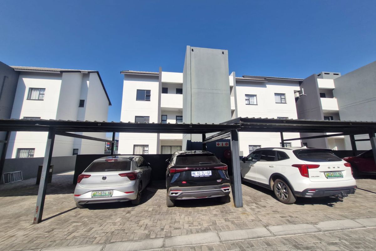 Modern apartment complex exterior featuring covered parking bays and paved driveway access.