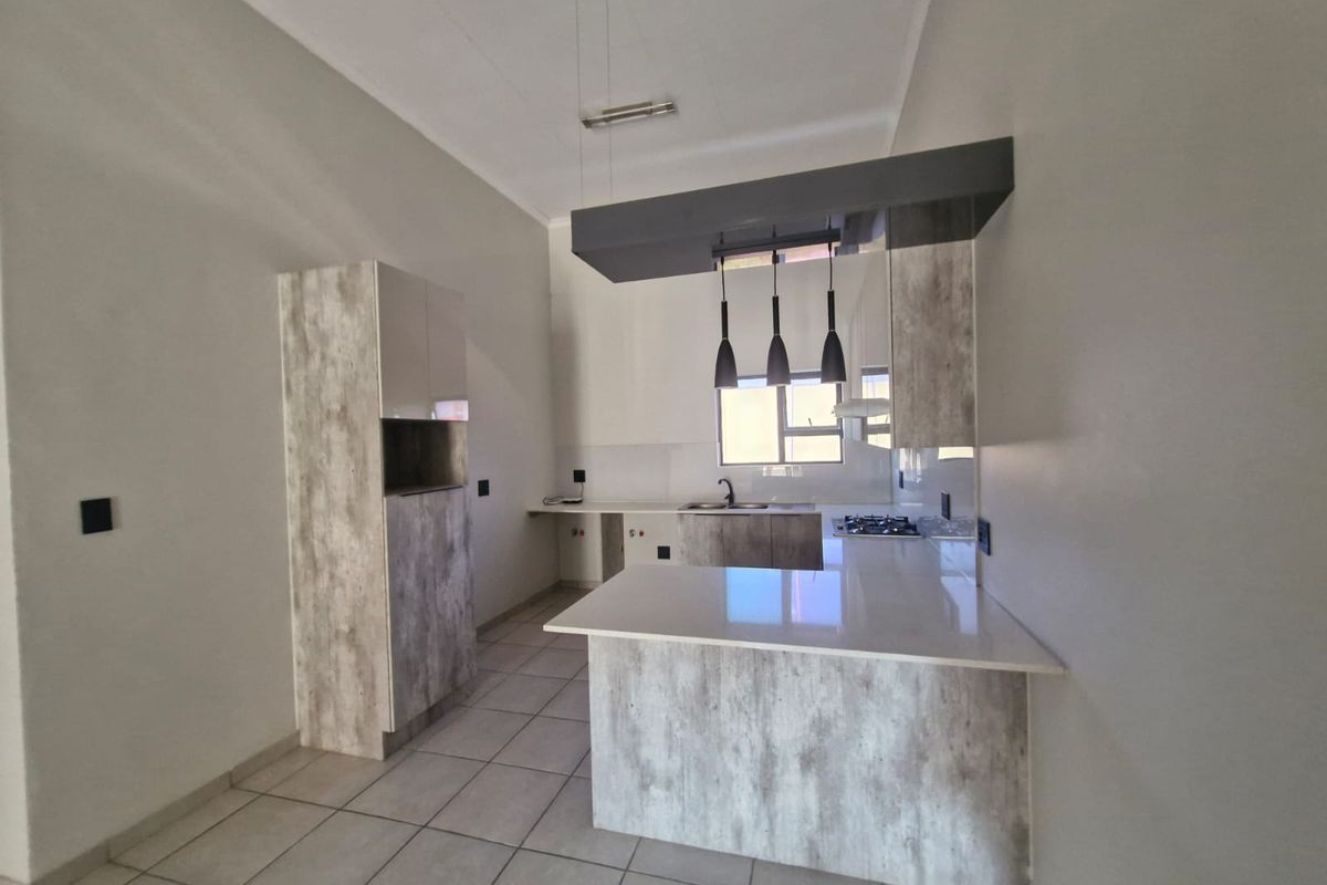 Modern kitchen featuring light wood-grain cabinetry, stone countertops, a gas hob, and a breakfast bar island with contemporary pendant lighting.