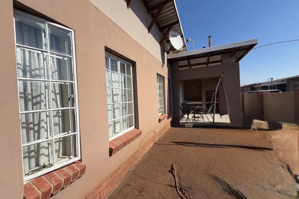 Rear view of the townhouse featuring a covered patio area and exterior facade with brick window sills, overlooking an unlandscaped yard.