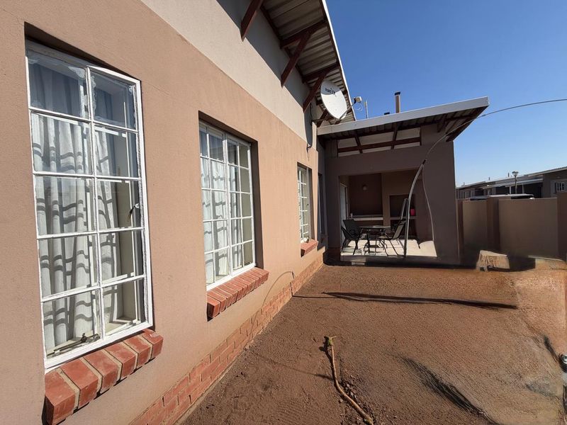 Rear view of the townhouse featuring a covered patio area and exterior facade with brick window sills, overlooking an unlandscaped yard.
