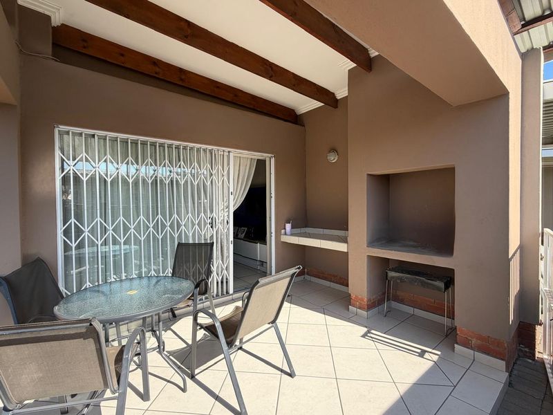 Covered patio featuring a built-in braai, tiled flooring, and exposed timber beams, providing a functional outdoor entertainment space.