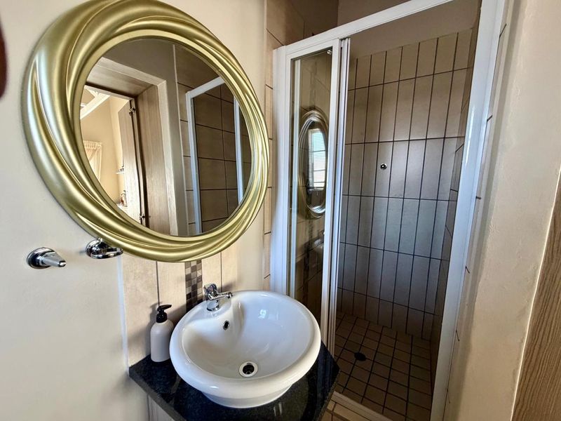A compact bathroom featuring a vessel sink on a granite vanity top and a separate shower enclosure with tiled walls.