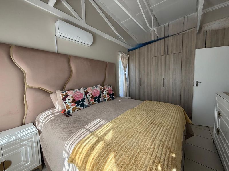 Bedroom featuring built-in cupboards, split-system air conditioning, and exposed roof trusses. The space requires minor finishing work around the ceiling area.