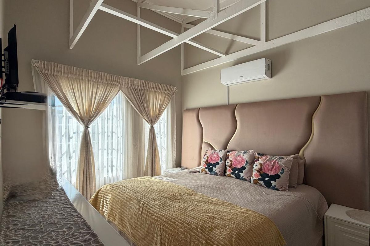 A well-maintained bedroom featuring exposed white ceiling trusses, a wall-mounted air conditioning unit, and a large upholstered headboard.
