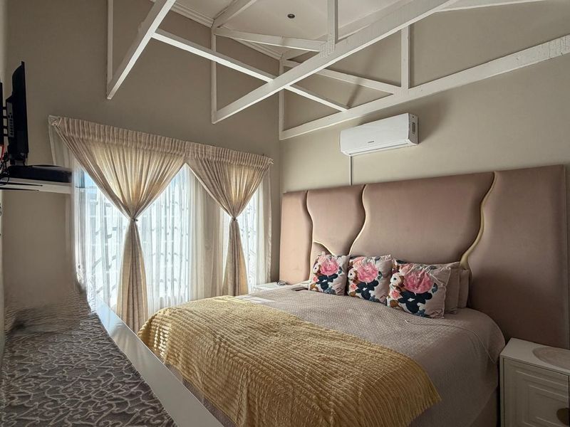 A well-maintained bedroom featuring exposed white ceiling trusses, a wall-mounted air conditioning unit, and a large upholstered headboard.
