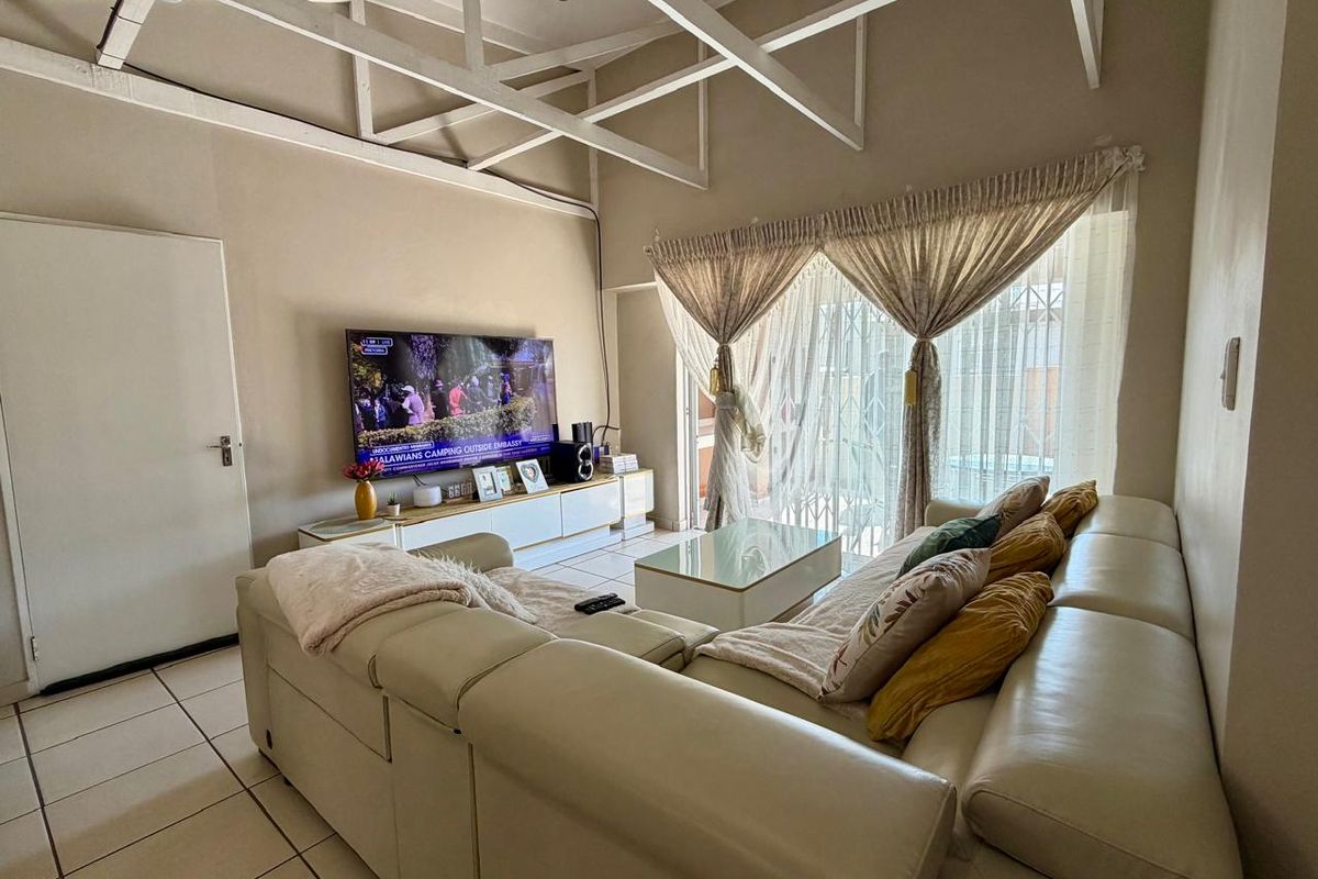 Spacious living room featuring high ceilings with exposed white trusses, ceramic tiled flooring, and direct access to an outdoor area through a sliding door.