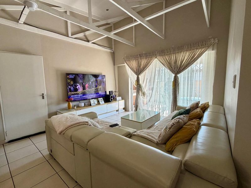 Spacious living room featuring high ceilings with exposed white trusses, ceramic tiled flooring, and direct access to an outdoor area through a sliding door.