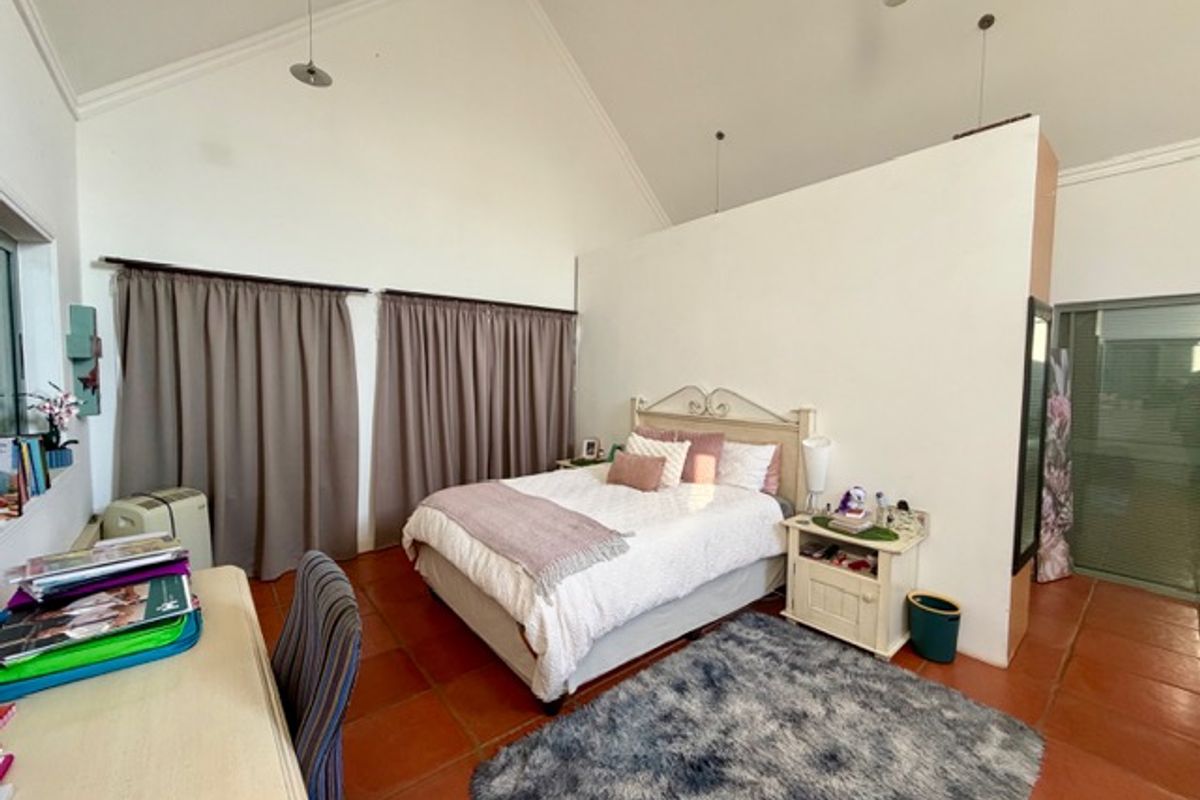 Spacious bedroom featuring a high vaulted ceiling, terracotta floor tiles, and a partial room divider wall.