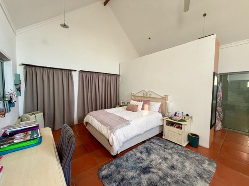 Spacious bedroom featuring a high vaulted ceiling, terracotta floor tiles, and a partial room divider wall.