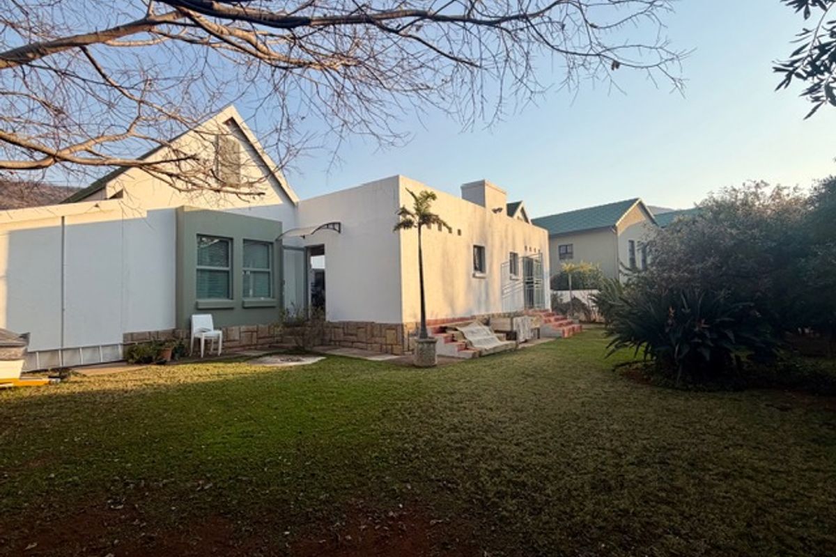 Rear view of the house featuring a lawn, landscaped garden, stone cladding accents, and concrete steps leading to the entrance.