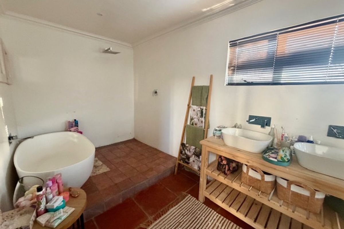 A spacious bathroom featuring a freestanding bathtub on a raised platform, double vessel sinks with wall-mounted taps, and classic terracotta floor tiling.