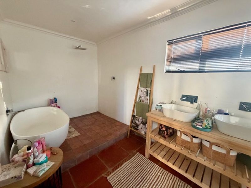 A spacious bathroom featuring a freestanding bathtub on a raised platform, double vessel sinks with wall-mounted taps, and classic terracotta floor tiling.