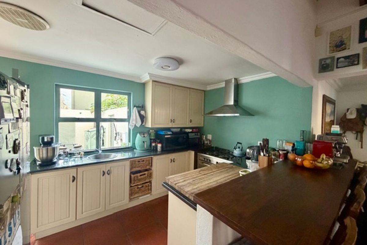A functional kitchen featuring built-in cabinetry, a stainless steel extractor fan, a gas hob, and a breakfast bar with terracotta flooring.