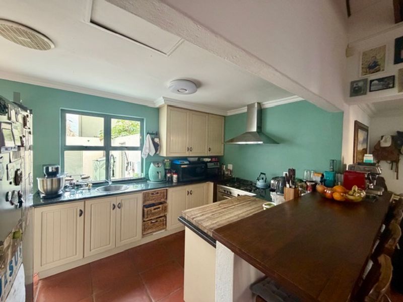 A functional kitchen featuring built-in cabinetry, a stainless steel extractor fan, a gas hob, and a breakfast bar with terracotta flooring.