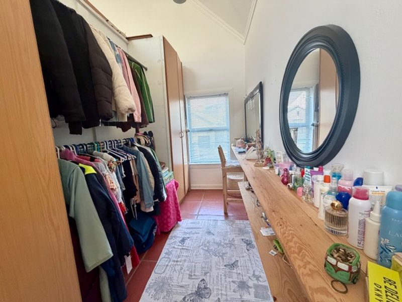 A functional dressing room or bedroom featuring built-in wardrobe storage, timber shelving, tiled flooring, and a vaulted ceiling.