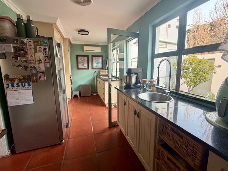 A functional kitchen featuring terracotta floor tiles, granite countertops, and built-in cabinetry, with a split-system air conditioner and natural light from large windows.