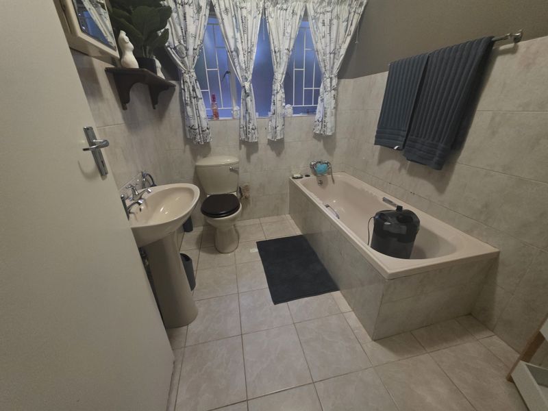 A functional bathroom featuring a pedestal basin, toilet, and built-in bathtub with tiled finishes and security bars on the window.