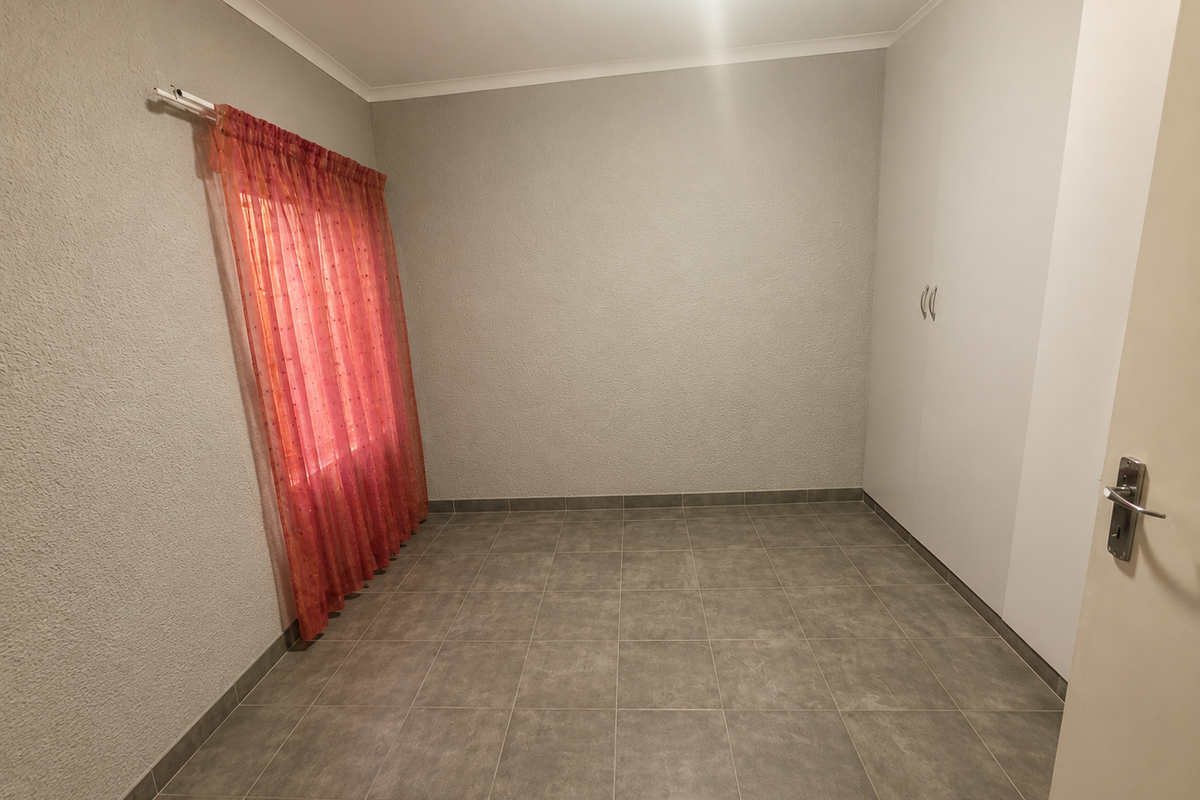 A clean, empty bedroom featuring neutral textured walls, tiled flooring, and a built-in wardrobe, providing a versatile space ready for personalization.