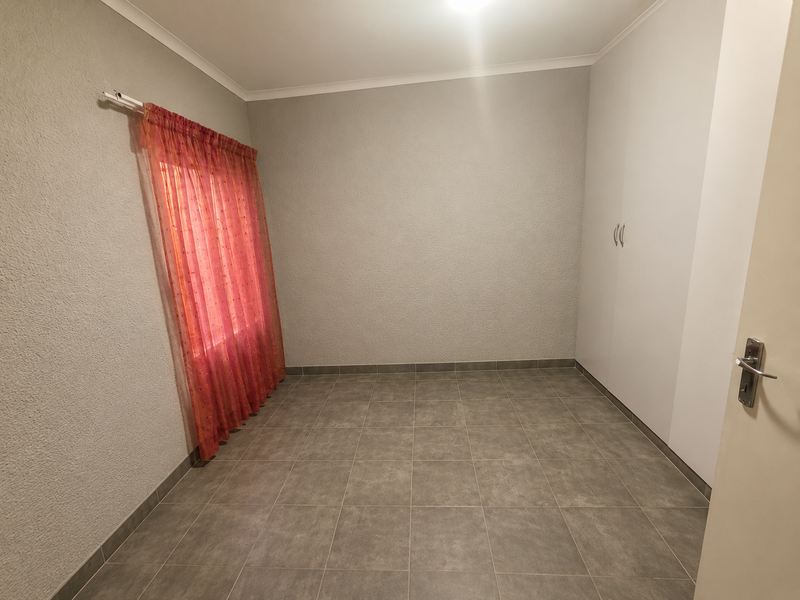 A clean, empty bedroom featuring neutral textured walls, tiled flooring, and a built-in wardrobe, providing a versatile space ready for personalization.