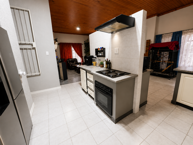 A functional kitchen area featuring a central island with a built-in oven, electric hob, and extractor fan, complemented by tiled flooring and a timber ceiling.