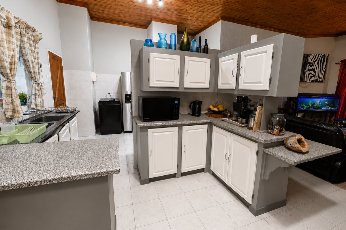 A functional kitchen featuring two-tone cabinetry, granite-look laminate countertops, double stainless steel sink, and a distinctive timber-paneled ceiling.