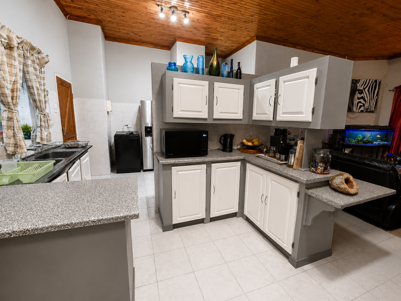 A functional kitchen featuring two-tone cabinetry, granite-look laminate countertops, double stainless steel sink, and a distinctive timber-paneled ceiling.