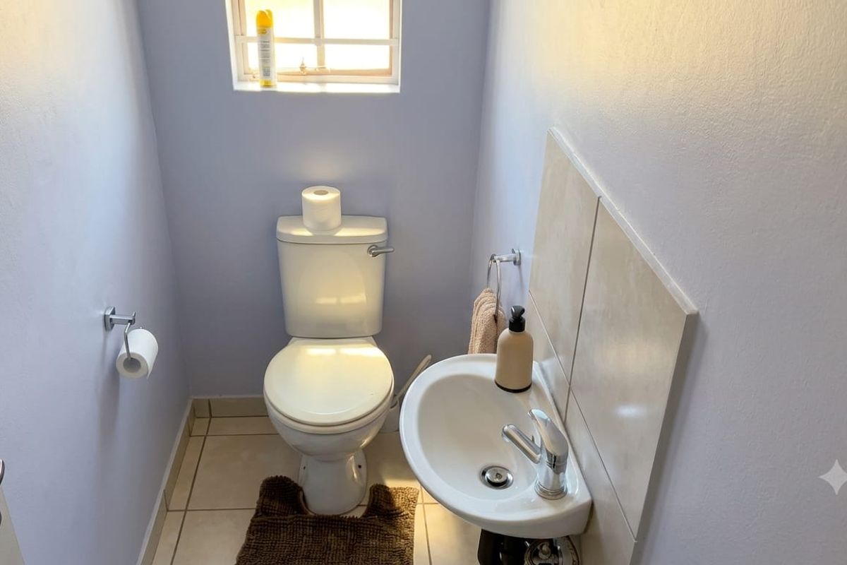 A compact guest bathroom featuring a white toilet, pedestal basin with mixer tap, and neutral tiled flooring.