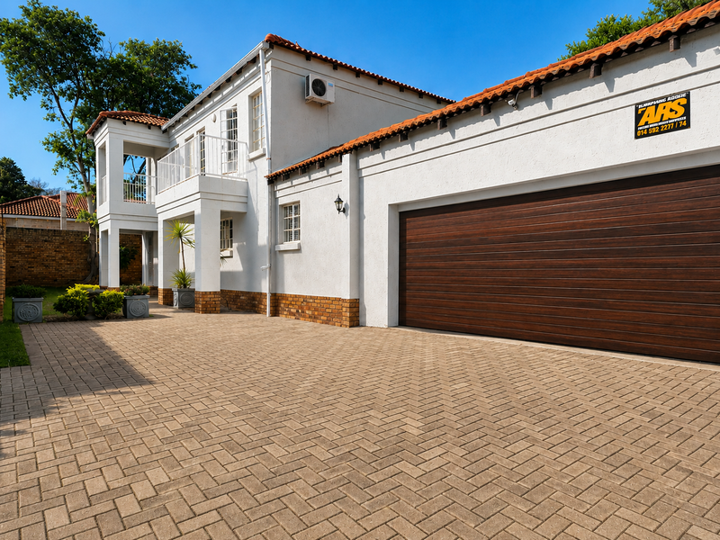 Front elevation of a two-story house featuring a paved driveway, double garage, and an upper-level balcony with terracotta roof tiles.