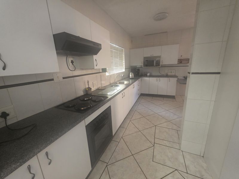 Functional kitchen featuring white cabinetry, dark countertops, built-in oven, electric hob, extractor fan, and tiled flooring throughout.