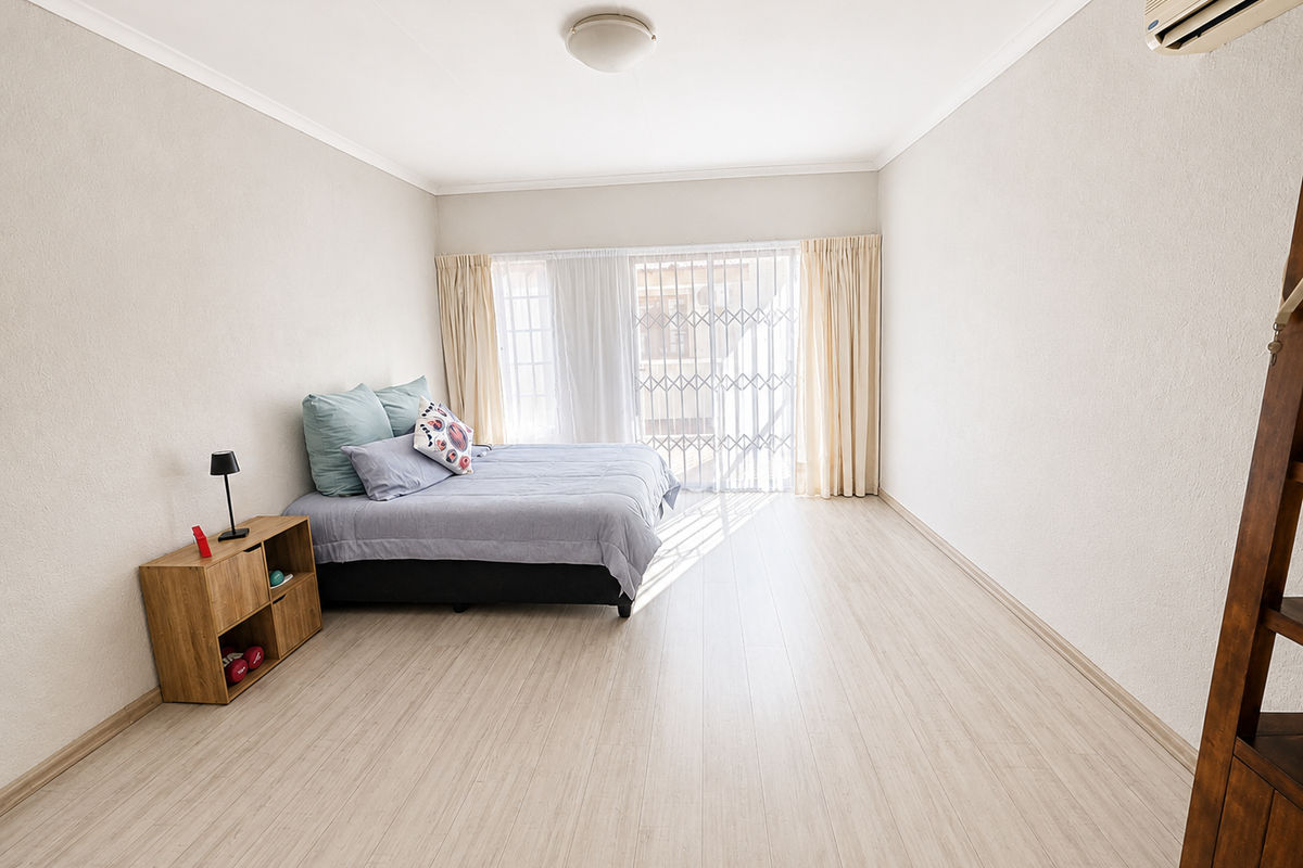 Spacious bedroom featuring light-toned laminate flooring, a wall-mounted air conditioning unit, and a sliding glass door with an integrated security gate.
