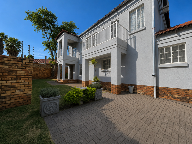 Rear view of a two-story house featuring a paved patio area, a balcony, and a well-maintained garden with brick boundary walls.